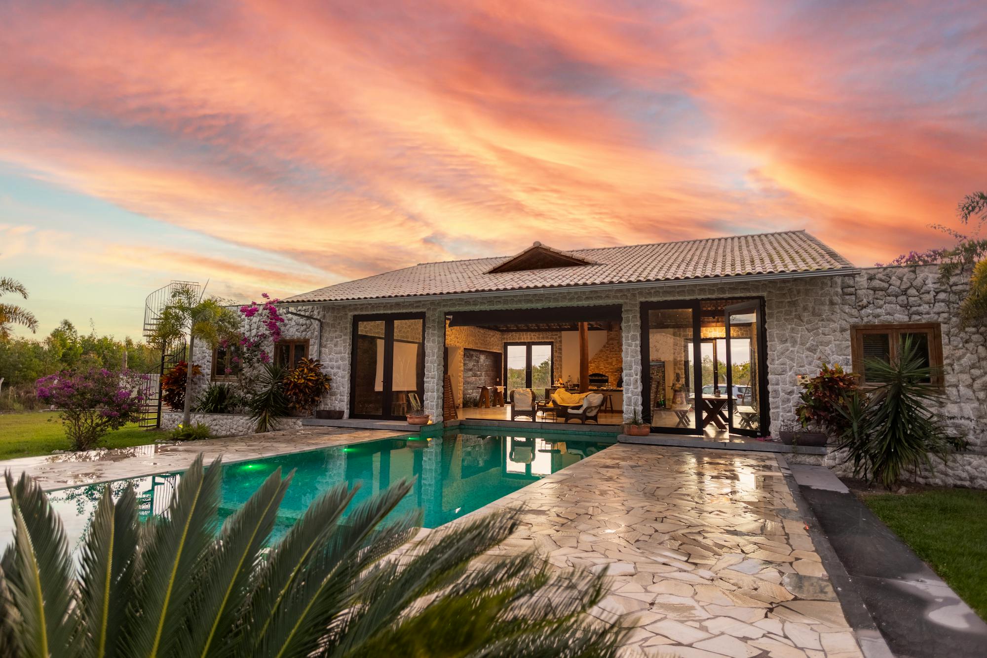 Dusk view of an illuminated backyard pool and patio