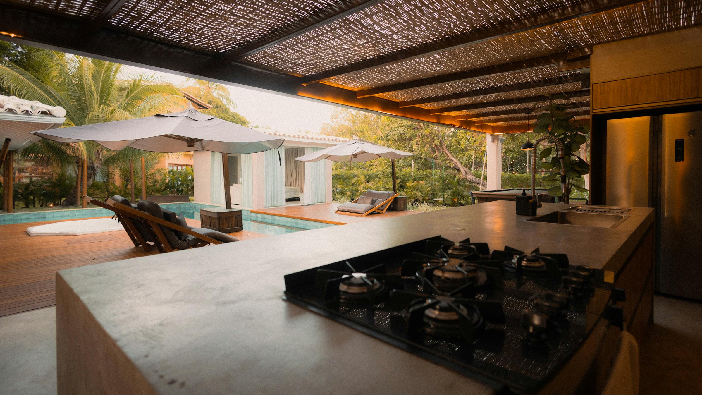 Pergola-covered outdoor kitchen overlooking a backyard pool at dusk